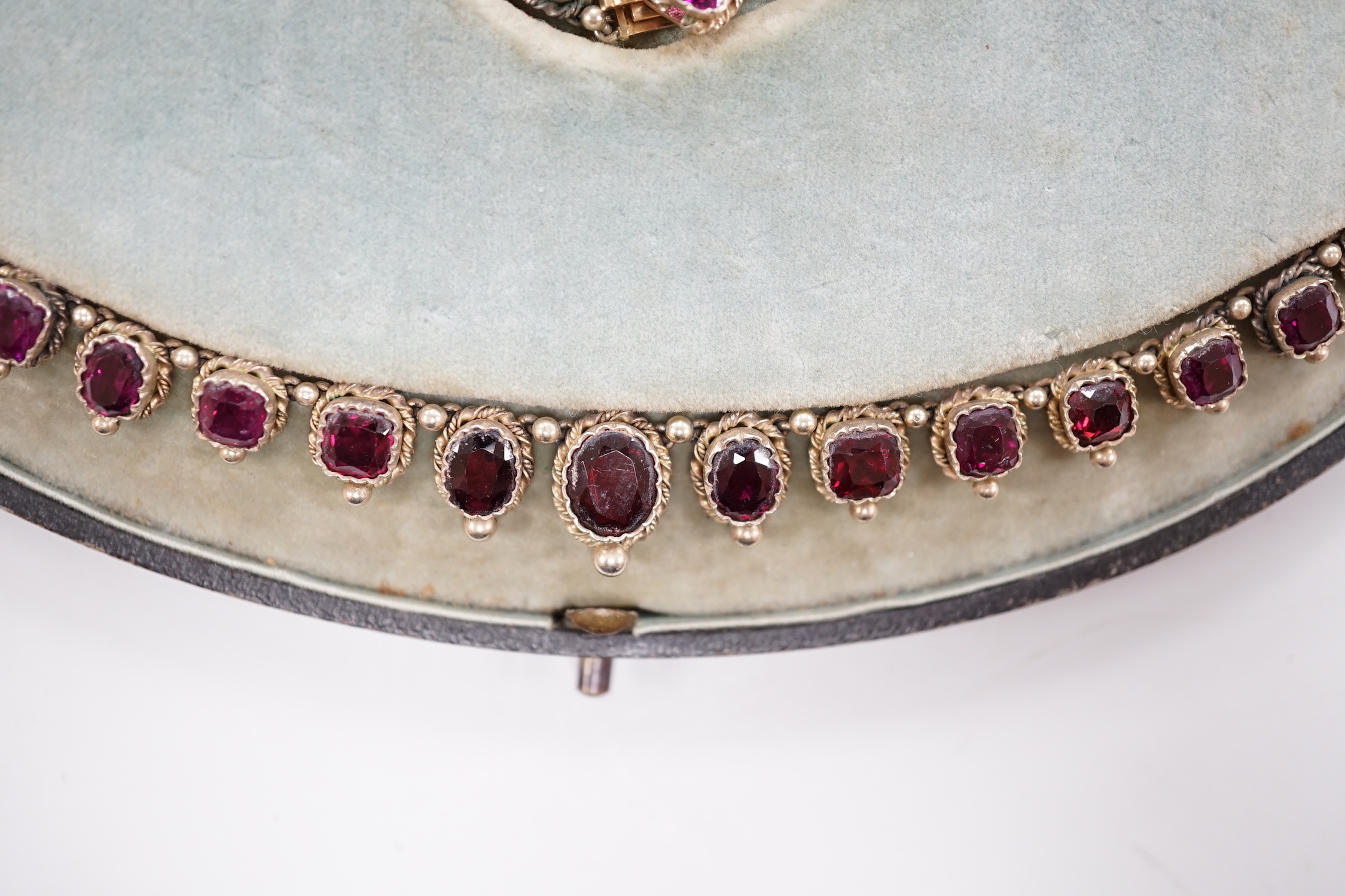 A cased 19th century gilt white metal and graduated oval and square cut garnet set fringe necklace, lacking drop, 37cm.